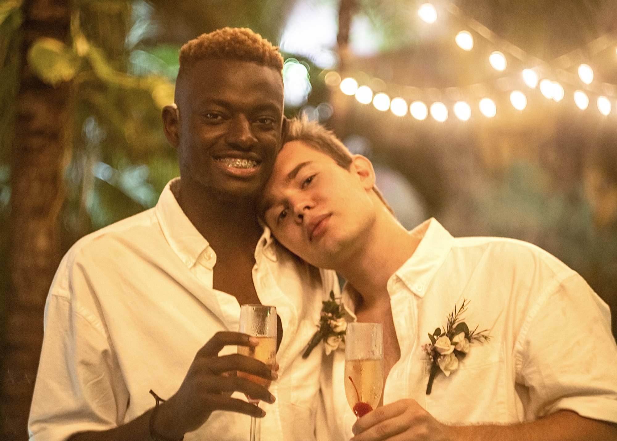 Two grooms at their candlelit wedding reception, one resting on the other, Riviera Maya